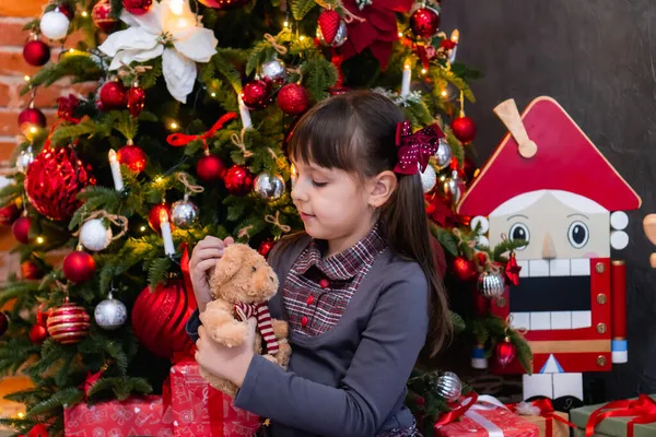 Noel ağacının yanındaki küçük beyaz kız yeni yıl için oyuncak ayı Noel 'i kutluyor. Fotoğraf serisi — Stok fotoğraf