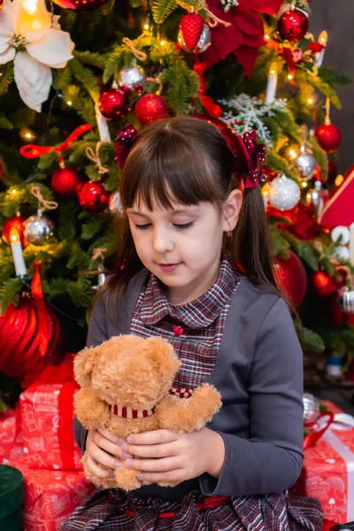 Noel ağacının yanındaki küçük beyaz kız yeni yıl için oyuncak ayı Noel 'i kutluyor. Fotoğraf serisi