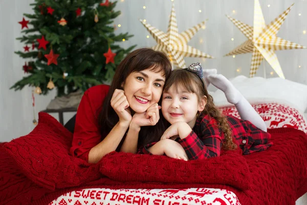 Noel konsepti. Mutlu anne-kız çocuğu Noel ağacının yanında yatıyor.