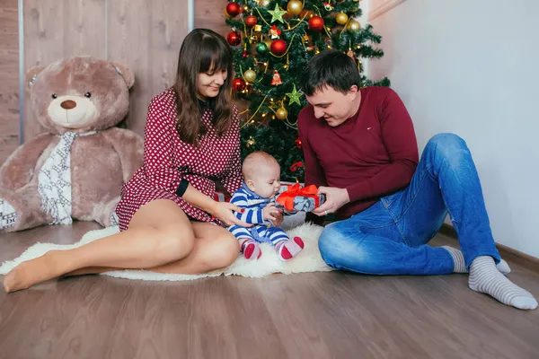 Noel 'i yeni yıl ağacının yakınında kutlayan genç bir aile. Küçük çocuk için hediye..