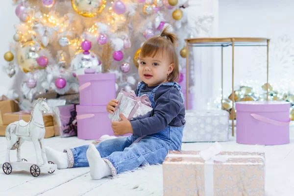 Şirin küçük kız, arka planda Noel ağacı süsleyen hediye kutusunu açıyor. — Stok fotoğraf