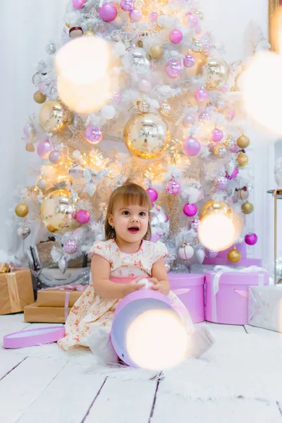 Şirin küçük kız, arka planda Noel ağacı süsleyen hediye kutusunu açıyor. — Stok fotoğraf