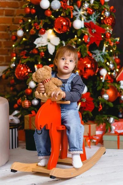Noel ağacının altında hediyelerle oyuncak ata binen güzel bir kız çocuğu. — Stok fotoğraf