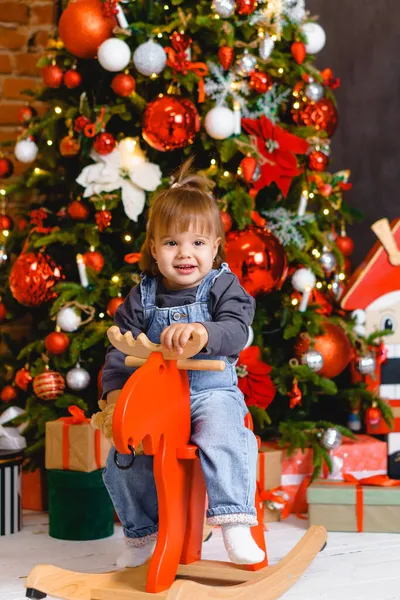 Noel ağacının altında hediyelerle oyuncak ata binen güzel bir kız çocuğu. — Stok fotoğraf