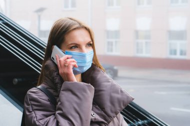 Tıbbi maske takan ve sokakta cep telefonuyla konuşan mutlu bir kadın. Koronavirüs covid-19 salgınına karşı koruma.
