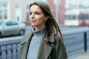 Şehir arka planında bulanık bir şekilde dışarıda yürürken düşünceli, şık bir kızın bakışları.