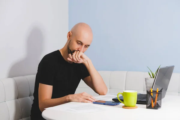 Thouthful kopasz férfi szakállas fekete pólóban dolgozik a noteszét otthon, oldalnézet — Stock Fotó