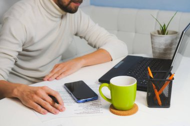 Beyaz boğazlı kazaklı adam evde defterin yanında çalışıyor. Üst görünüm