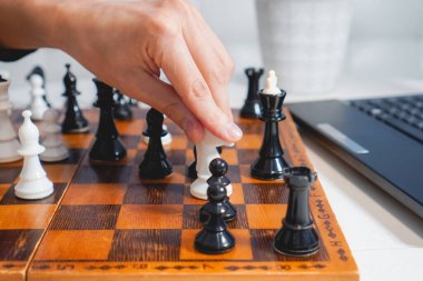 Adam dizüstü bilgisayarın yanında tahta tahtada satranç oynuyor. Üst Manzara. Seçici odaklanma. Strateji ve rekabet kavramı