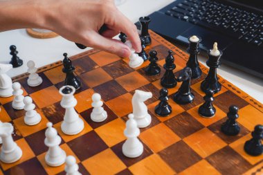 Adam dizüstü bilgisayarın yanında tahta tahtada satranç oynuyor. Üst Manzara. Seçici odaklanma. Strateji ve rekabet kavramı