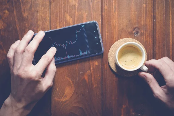 Akıllı cep telefonunda grafiği olan bir adam telefona dokunuyor. İş ve finansal konsept. Kahve hazır.