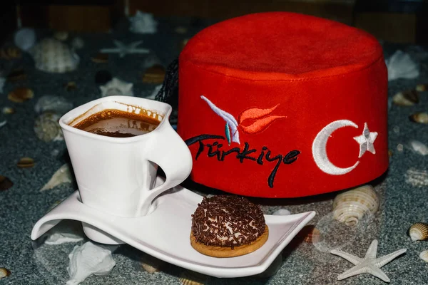 Üzerinde fes ve deniz kumu olan Türk kahvesi ve kurabiyesi. Kırmızı Türk şapkalı beyaz kahve fincanı.