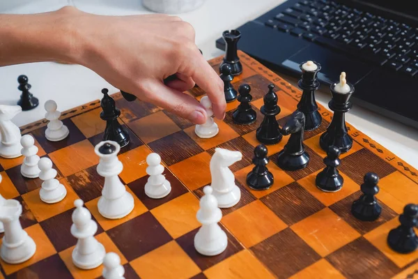 Adam dizüstü bilgisayarın yanında tahta tahtada satranç oynuyor. Üst Manzara. Seçici odaklanma. Strateji ve rekabet kavramı