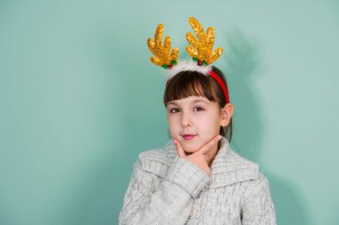 Nane arkaplanda izole edilmiş sarı geyik boynuzları takan düşünceli bir kızın stüdyo portresi.