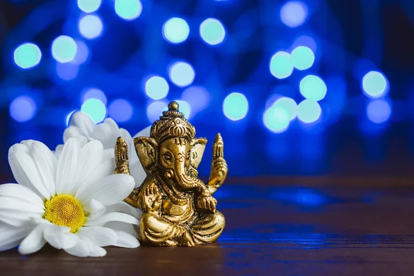 Golden lord ganesha skulptur i tusensköna blommor över blå belyst bakgrund. Kopiera utrymme för text — Stockfoto