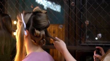 Kuaför, kuaförde saç spreyi kullanan genç sarışın kadına saç stili yapıyor.