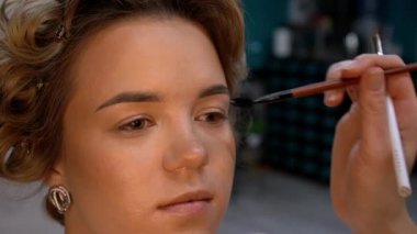 Kaş makyajı mı? Profesyonel makyöz, genç bir kadının kaşlarını düzeltmek için fırça kullanır.