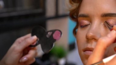 Profesyonel makyöz, genç bir kadının göz kapağına göz farı sürüyor. Kapat.