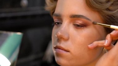 Profesyonel makyöz, genç bir kadının göz kapağına göz farı sürüyor. Kapat.