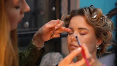 Profesyonel makyöz, genç bir kadının göz kapağına göz farı sürüyor. Kapat.