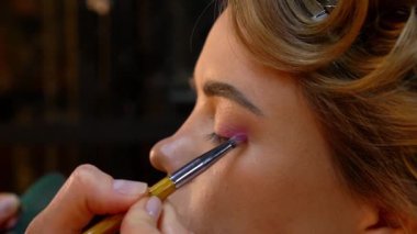 Profesyonel makyöz, genç bir kadının göz kapağına göz farı sürüyor. Kapat.