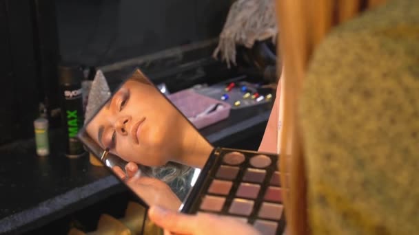 Επαγγελματική make-up καλλιτέχνης εφαρμόζει σκιά ματιών στο βλέφαρο της νεαρής γυναίκας. Κλείσε. — Αρχείο Βίντεο
