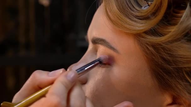 El maquillador profesional aplica la sombra de ojos al párpado de la mujer joven. De cerca. — Vídeos de Stock