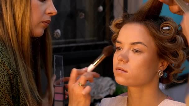 Friseur und Visagist mit Pinsel und Palette machen Frisur und Make-up für junge Frau — Stockvideo