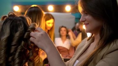 Kuaför, güzellik salonundaki genç sarışın kadına kıvırcık saç stili yapıyor. Moda kavramı