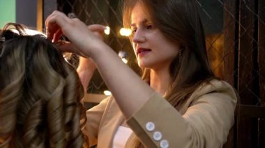 Kuaför, güzellik salonundaki genç sarışın kadına kıvırcık saç stili yapıyor. Moda kavramı