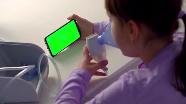 Kleines Mädchen ist krank, inhaliert mit Vernebler und schaut auf Handy mit Green-Screen-Attrappe — Stockvideo