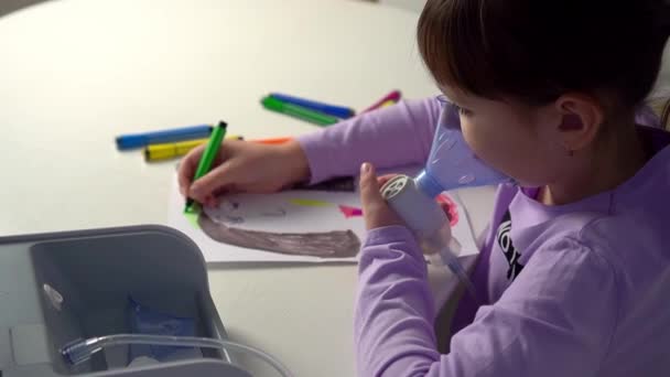 Klein meisje maakt inhalatie met medische vernevelaar terwijl ze aan tafel zit en tekent met stiften — Stockvideo