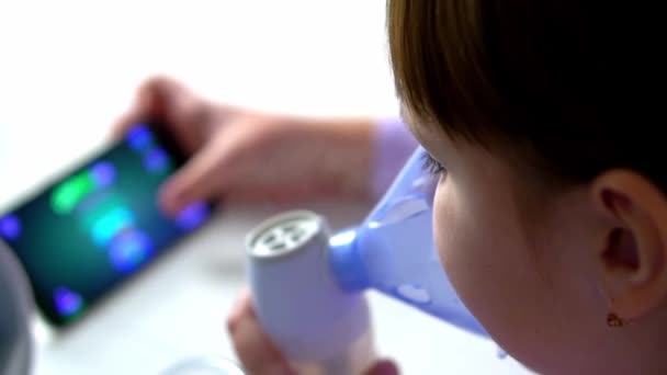 Küçük kız hasta, nebulizörle soluyor ve martphone ile oyun oynuyor. — Stok video
