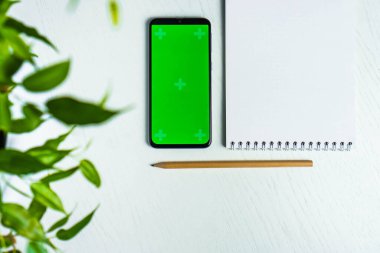 Yeşil izin, boş not defteri, akıllı telefon, yeşil ekran modeli ve düz kalem. Üst görünüm
