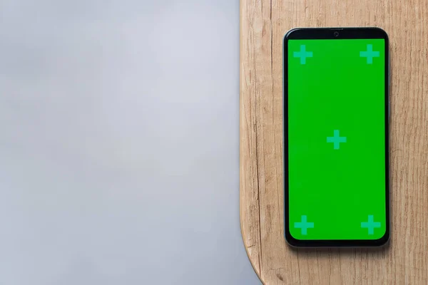 Smartphone s prázdným zeleným displejem mockup na dřevěném pozadí s kopírovacím prostorem — Stock fotografie