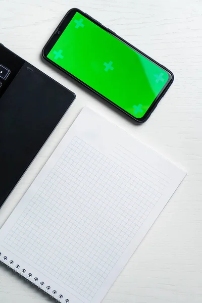 Λευκό φορητό υπολογιστή σημειωματάριο και πράσινο smartphone οθόνη σε λευκά τραπέζια, αντίγραφο χώρου, επίπεδη lay, κορυφαία προβολή, mock up — Φωτογραφία Αρχείου