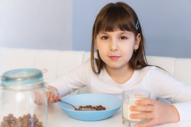 Küçük kız beyaz masada oturmuş sütlü çikolatalı mısır topu yiyor. Çocuk kahvaltı yapıyor.