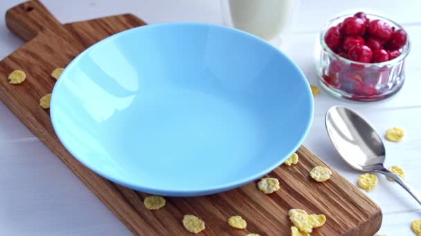 Płatki kukurydziane są wlewane do niebieskiej miski na drewnianym stole. Płatki kukurydziane mleko i wiśnia zdrowe śniadanie — Wideo stockowe