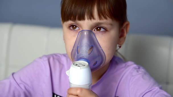 La niña pequeña inhala con un nebulizador médico mientras está sentada en la mesa. De cerca. — Vídeos de Stock