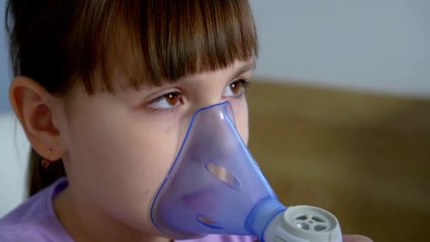 Маленька дівчинка робить інгаляцію з медичним небулайзером, тримаючи маску на обличчі вдома — стокове відео