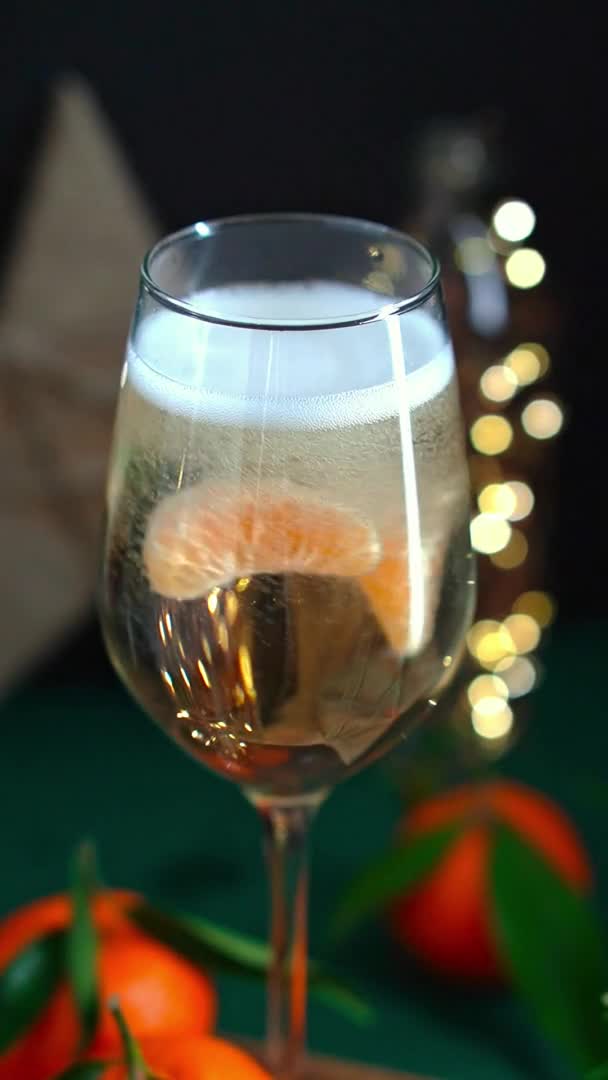 Tangerine slices swirl in wineglass full of sparkling wine with mandarins fir brunch and garland — Stock Video