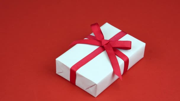 Κορίτσι χέρια λάβει λευκό κουτί δώρου με κόκκινο τόξο στο κόκκινο τραπέζι διακοσμημένα με καρδιά. Ημέρα του Αγίου Βαλεντίνου — Αρχείο Βίντεο