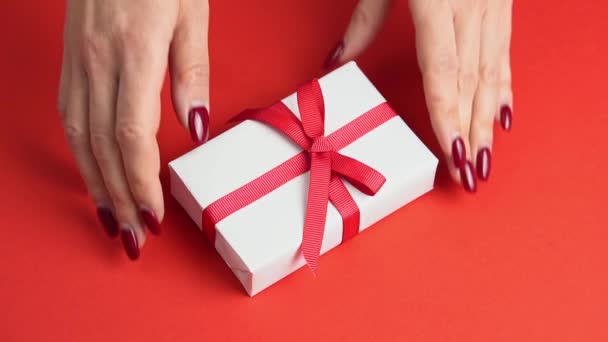 Woman hands take white gift box with red bow on red table decorated with heart. Valentines day — Stock Video