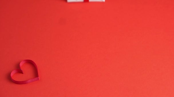 Le mani di donna mettono la scatola di regalo bianca con inchino rosso su tavolo rosso decorato con cuore. San Valentino — Video Stock