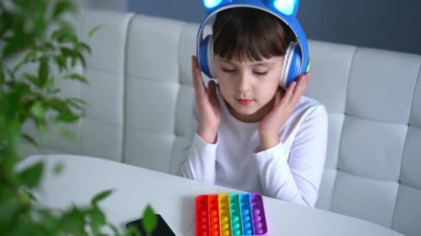 Baby meisje spelen met regenboog pop het fidget en het luisteren naar muziek met hoofdtelefoon — Stockvideo