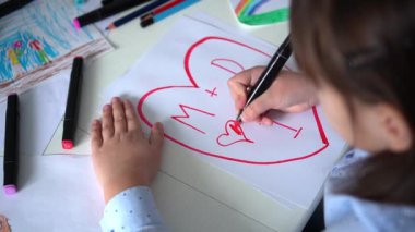 Çocuk pembe kalemlerle kağıt üzerine kalp çizer. Çocukların yaratıcılığı. Sevgililer Günü, mutlu aile.