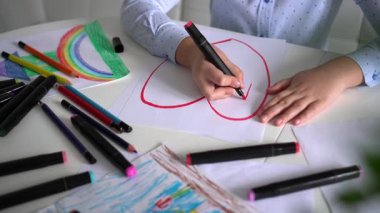 Çocuk pembe kalemlerle kağıt üzerine kalp çizer. Yakın plan. Çocukların yaratıcılığı. Sevgililer Günü