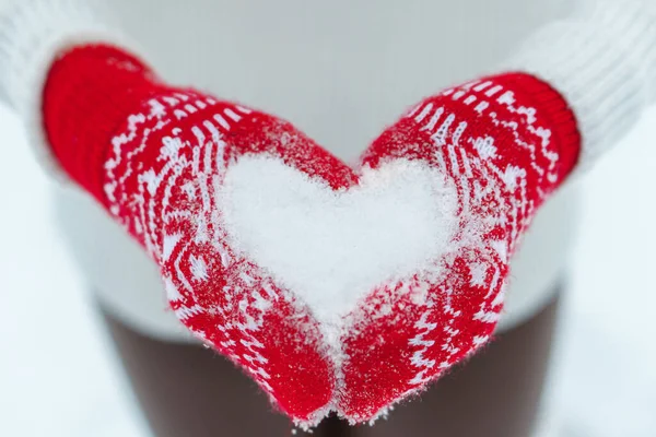 Γυναικεία χέρια σε πλεκτά γάντια με καρδιά από χιόνι την ημέρα του χειμώνα. Αγάπη ή Ημέρα του Αγίου Βαλεντίνου έννοια Royalty Free Φωτογραφίες Αρχείου