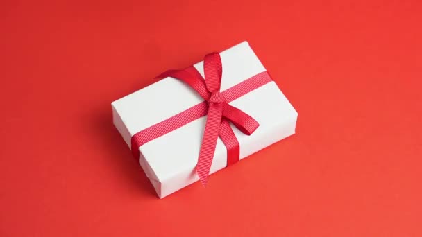 Kadın elleri, kırmızı masa üzerindeki kırmızı kurdeleli beyaz hediye kutusunu alır. Sevgililer Günü — Stok video