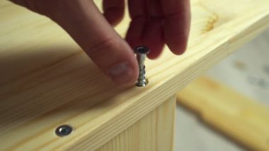 Mobilya montajı. Sanatçı, tahta tahtaya elektrikli tornavidayla vida sokuyor.